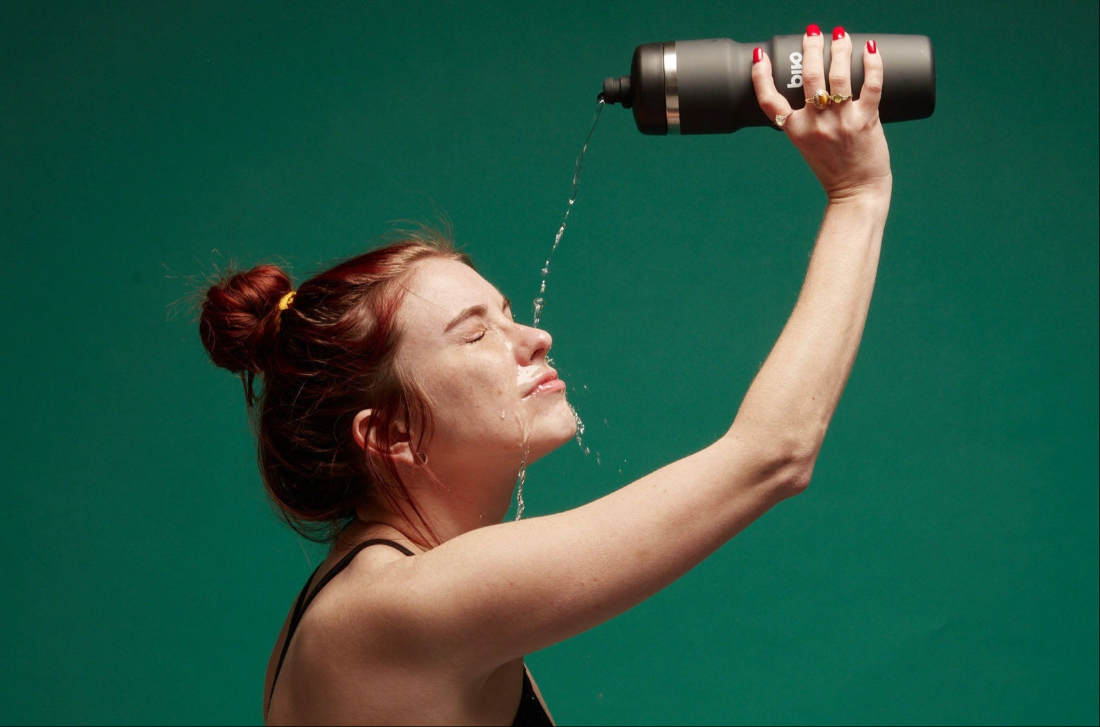 Kira pouring water on her head from an insulated stainless steel Bivo bottle in black.