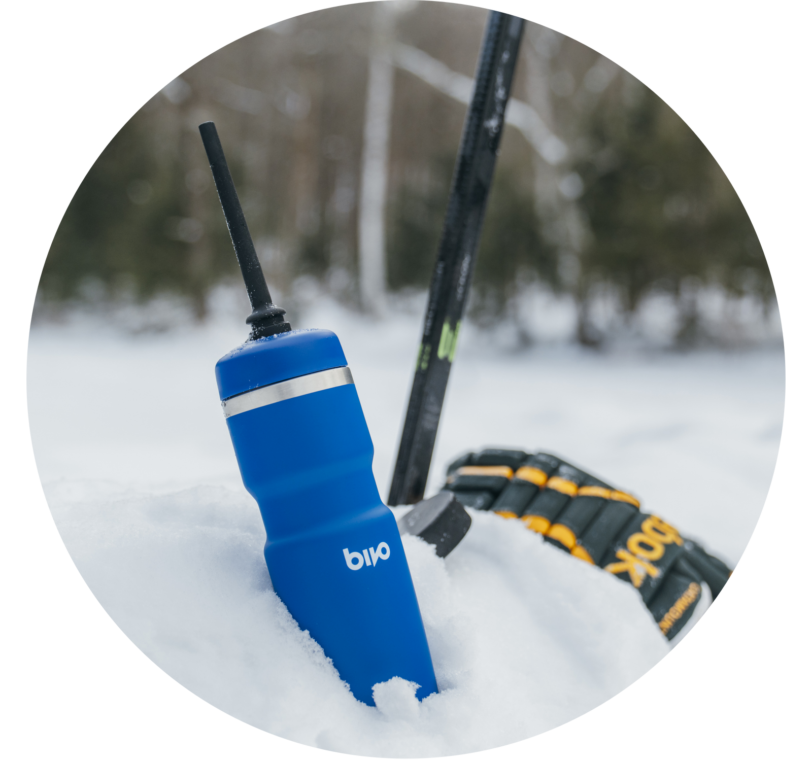 Blue water bottle in the snow with hockey gear behind it.