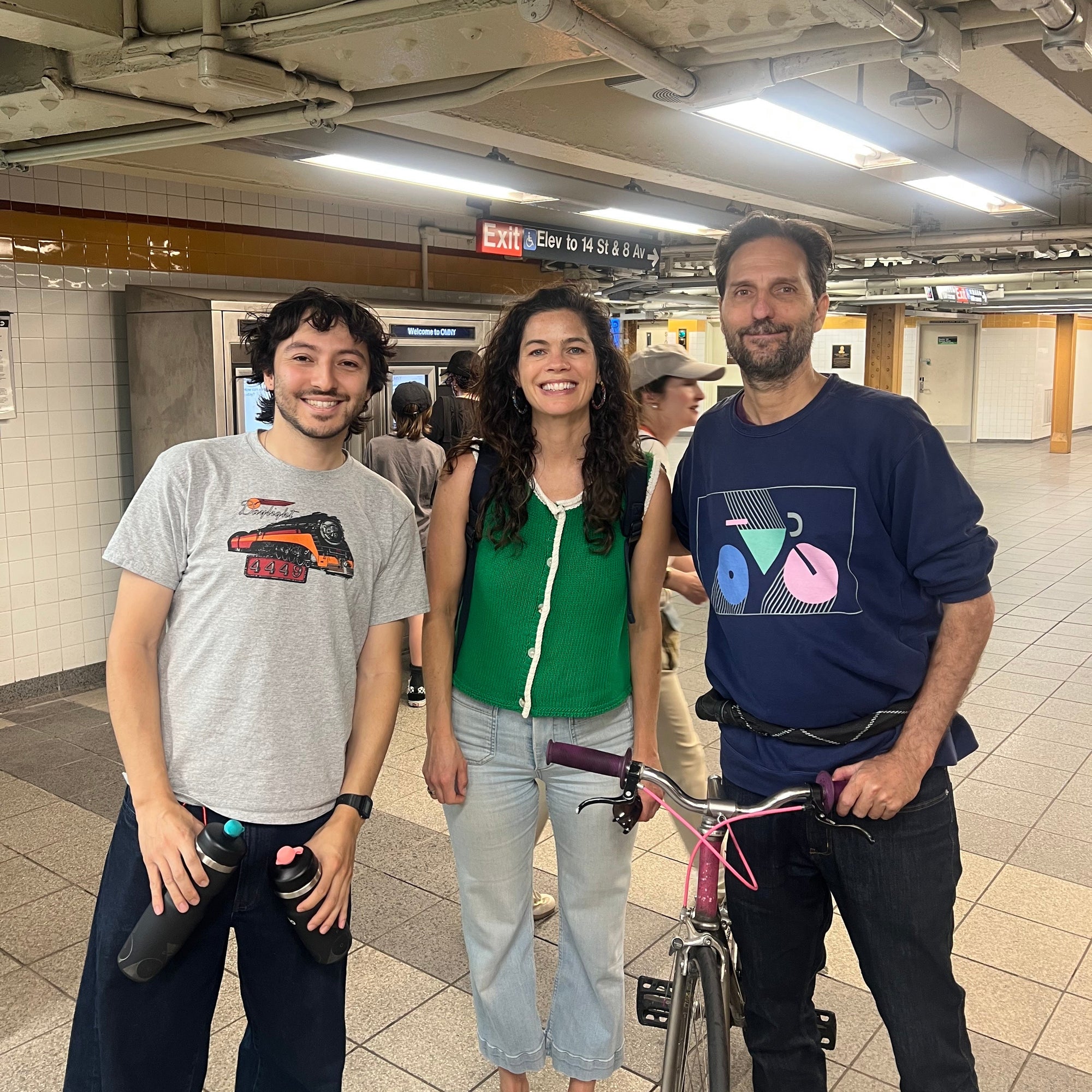 Three people standing together in a subway station with one person holding a bicycle.