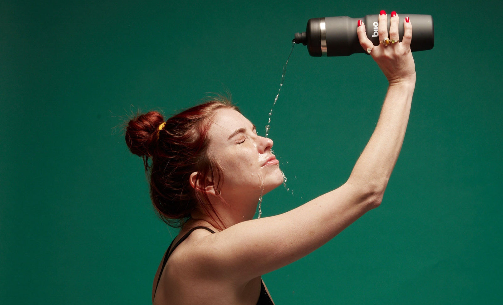 A woman pouring water on her head from an insulated stainless steel bottle