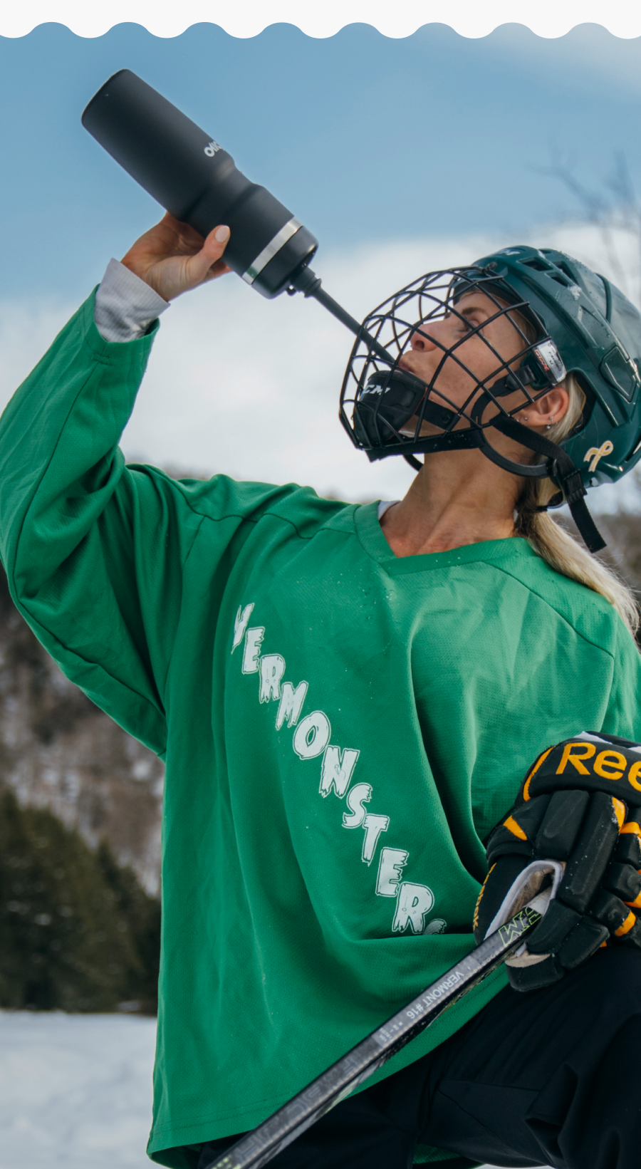 Person in green sports jersey holding a black water bottle with a snowy background