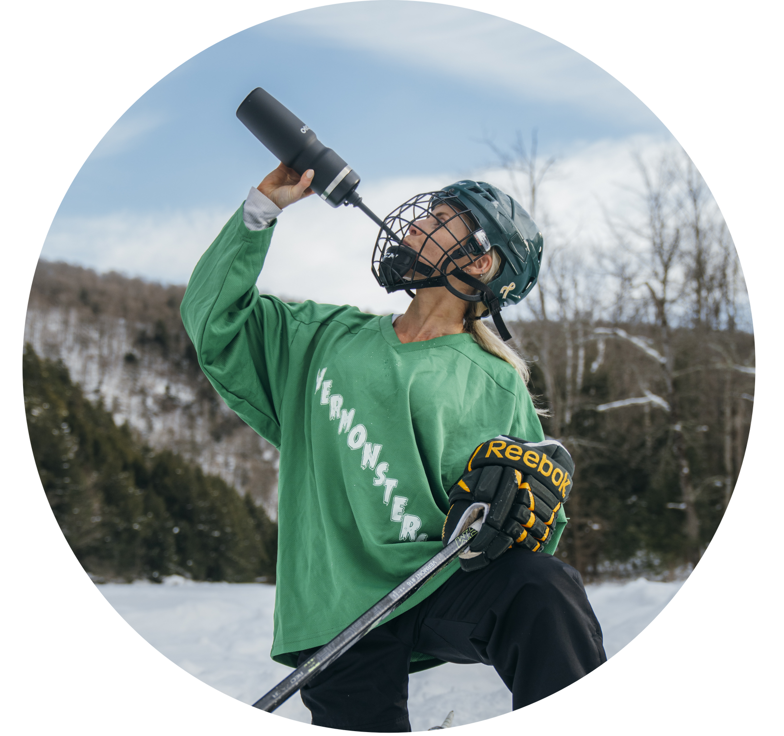 Person in green hockey jersey and helmet holding a hockey stick outdoors in winter.