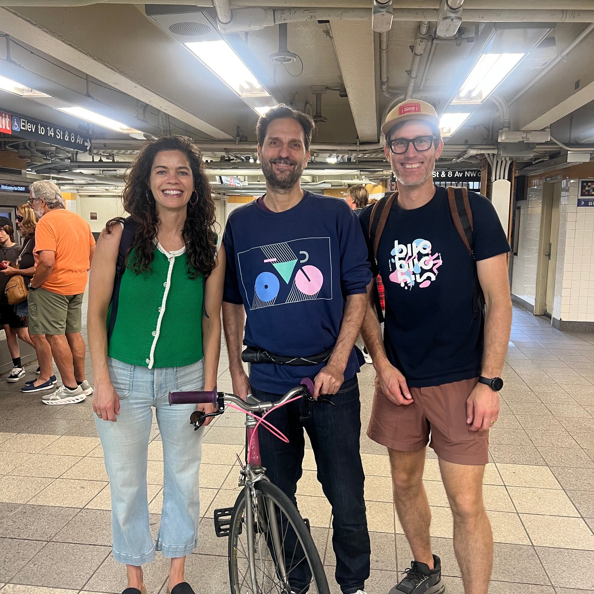 Three people standing in a subway station with a bicycle