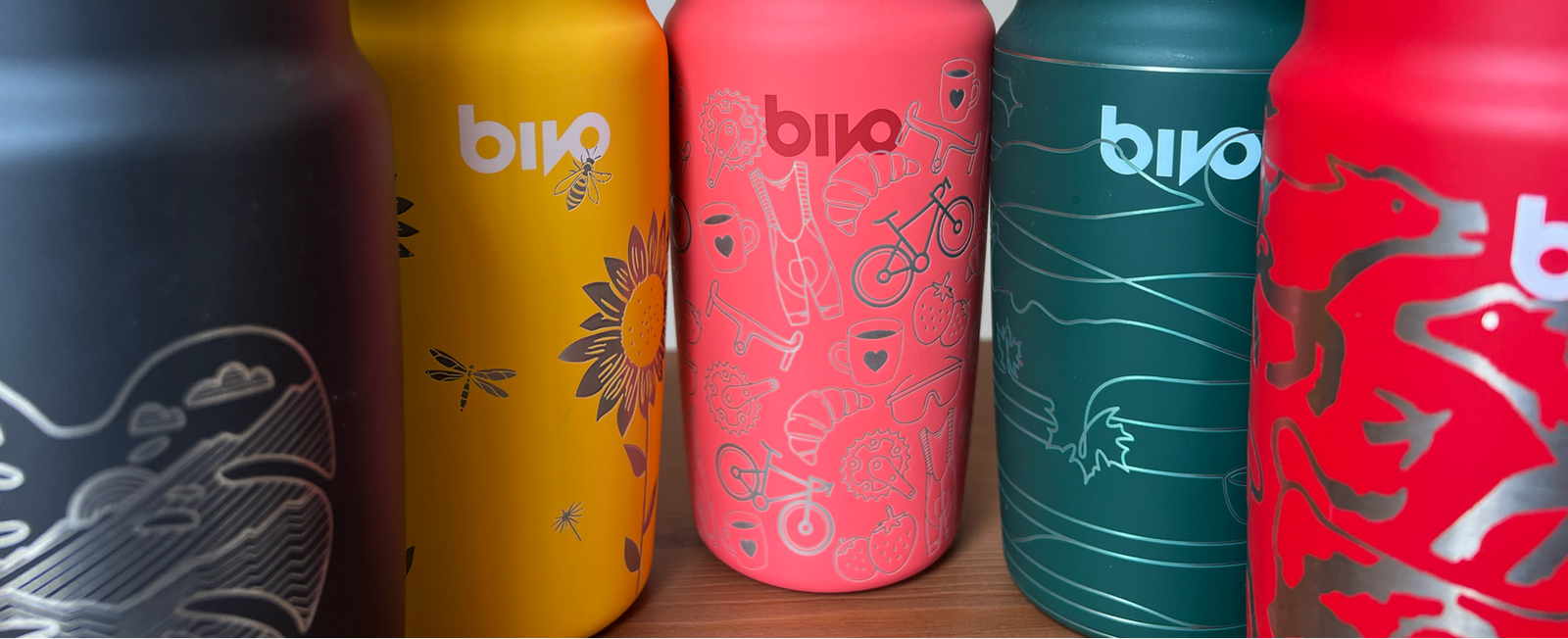 Five colorful water bottles with 'Bivo' branding on a wooden surface.