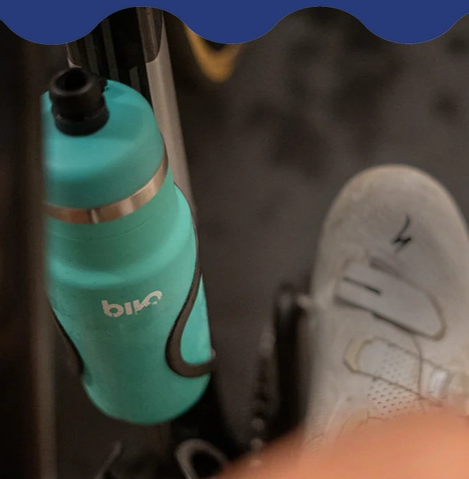 Teal Bivo water bottle with black cap attached to a metal surface, blurred background